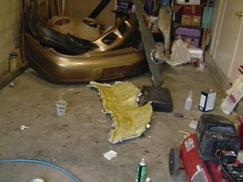 1999 Ford Taurus - Car bumper and fiberglass mat on a garage floor with tools and an air compressor.