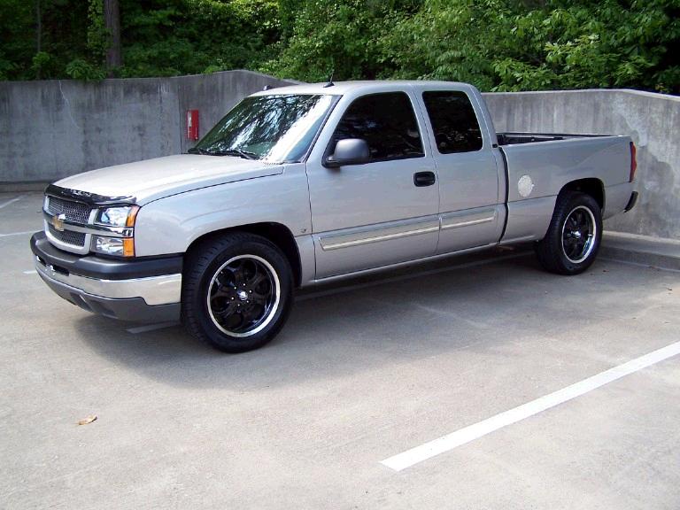 Silver Chevrolet Silverado extended-cab pickup with black aftermarket wheels in a parking deck