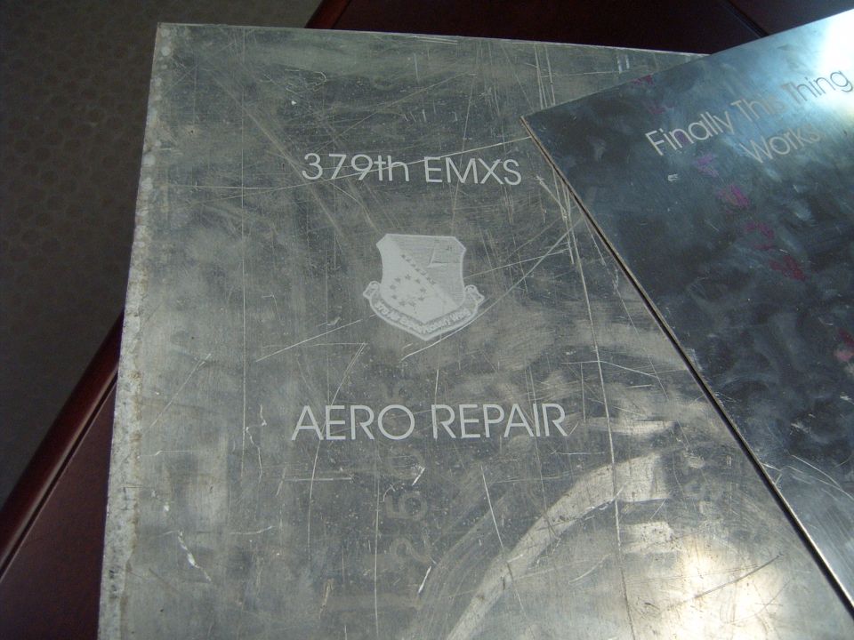 Metal plaque with '379th EMXS' and 'AERO REPAIR' text, plus an emblem. Another metal sheet is partially covering it