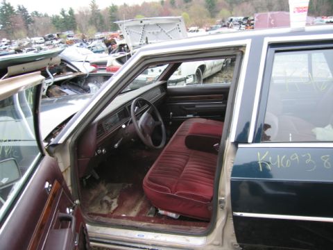 1991 Ford LTD Crown Victoria - The interior of a dark blue Ford Crown Victoria, showing the maroon velour seats and dashboard. Yard cars are visible in the background.