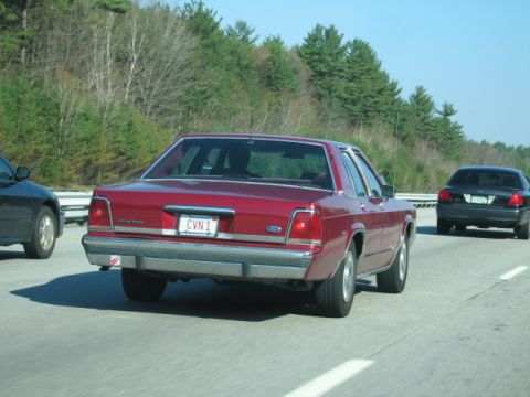 1991 Ford LTD Crown Victoria - A red 1991 Ford Crown Victoria is seen from the rear on a highway, with a black car following closely behind.