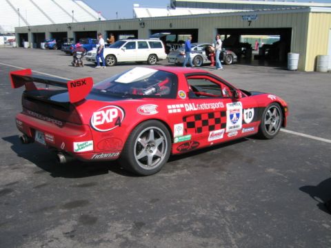 1991 Ford LTD Crown Victoria - A red sports car with racing decals and a large rear spoiler is parked at a racetrack.