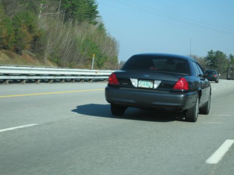 1991 Ford LTD Crown Victoria - Rear view of a dark sedan driving on a highway, with other vehicles visible in the distance.