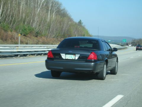 1991 Ford LTD Crown Victoria - Rear view of a dark sedan on a highway under a clear blue sky.