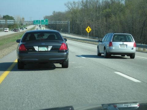 1991 Ford LTD Crown Victoria - A dark sedan is seen from behind on a highway, with another car in the adjacent lane.