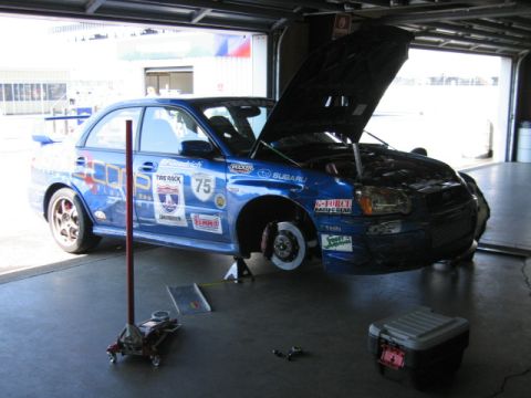 1991 Ford LTD Crown Victoria - A blue Subaru Impreza WRX STI race car is shown with its hood open, elevated on jacks inside a garage bay.