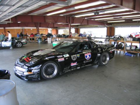 1991 Ford LTD Crown Victoria - A black race car is parked in a garage, covered in various sponsor decals and racing numbers.