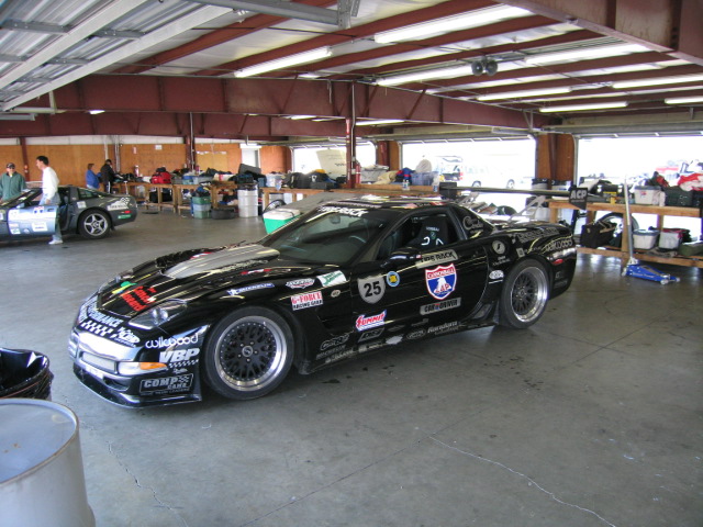 Black race car with many sponsor stickers and racing number 25 inside a garage