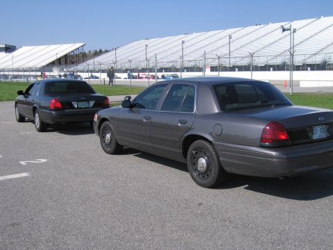 1991 Ford LTD Crown Victoria - Two Ford Crown Victoria sedans are parked on a paved surface near grandstands.