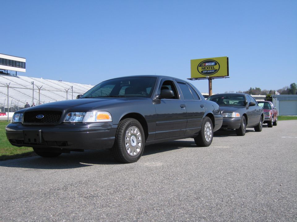 Dark gray sedan parked in a line with other cars, NASCAR Nextel billboard in background