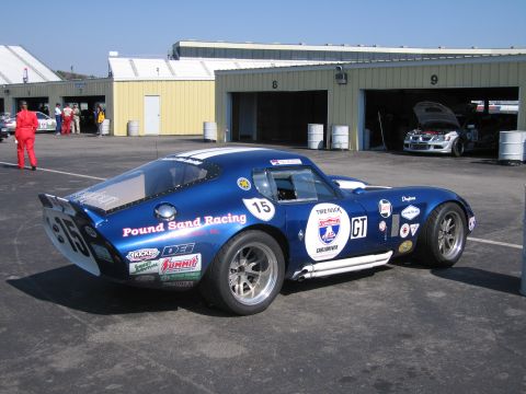 1991 Ford LTD Crown Victoria - A blue racing car with the number 15 is parked at a track, with garages and other vehicles in the background.