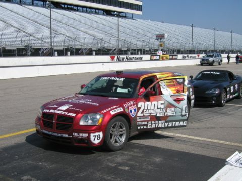 1991 Ford LTD Crown Victoria - A red Dodge Magnum, labeled as a 2005 Cannonball Run race vehicle, sits on a race track next to a black sports car.