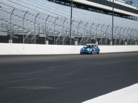 1991 Ford LTD Crown Victoria - A blue Mini Cooper drives on a race track with empty stadium seating in the background.
