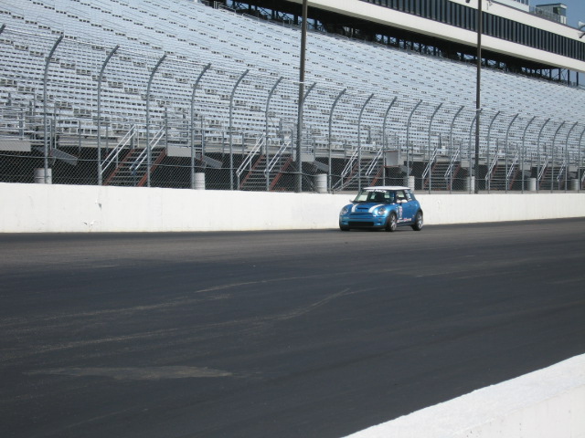Blue Mini Cooper on a race track in front of stadium seating