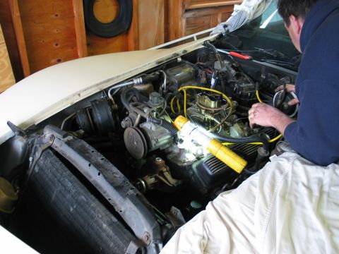 1981 Chevrolet Corvette - A person works on the engine of a white 1981 Chevrolet Corvette in a garage.