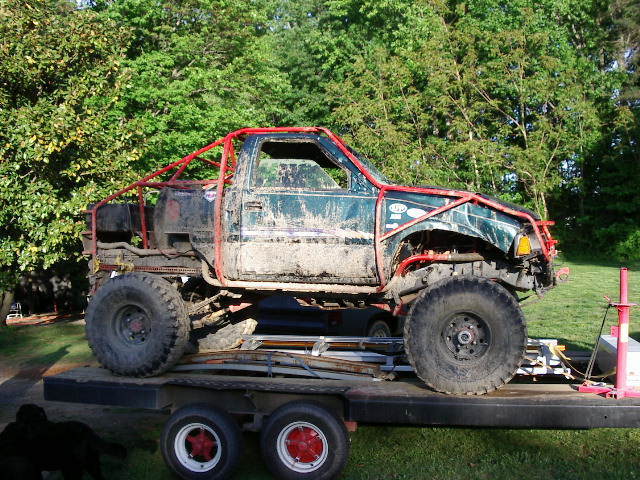 Mud-covered off-road truck with red roll cage on trailer