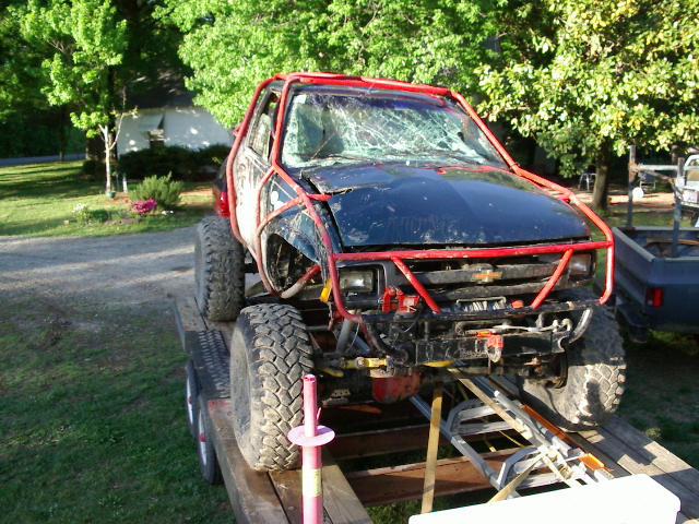Modified off-road truck with red roll cage and cracked windshield on a trailer
