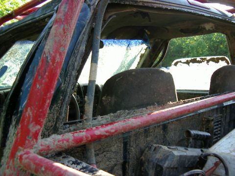 1985 Ford Bronco - The interior of this vehicle is heavily covered in mud, with a roll cage and a cracked windshield visible.