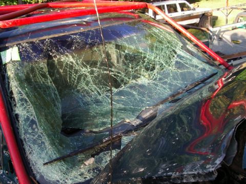 1985 Ford Bronco - Vehicle windshield is heavily damaged with a red roll cage visible.
