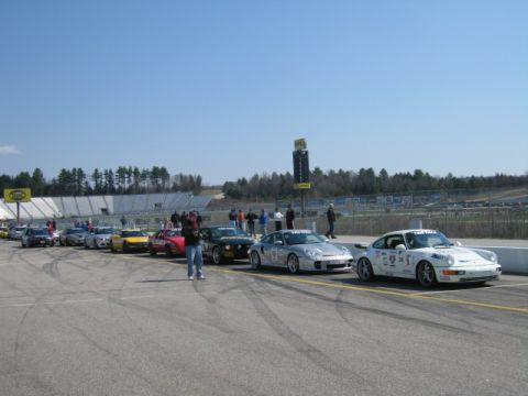 1991 Ford LTD Crown Victoria - Sports cars are lined up on a racetrack, ready for an event, with a scoreboard visible.