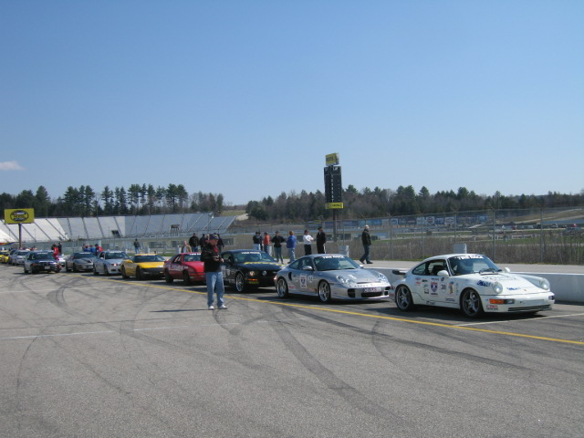 Several sports cars lined up on a racetrack with spectators and a scoreboard in the background