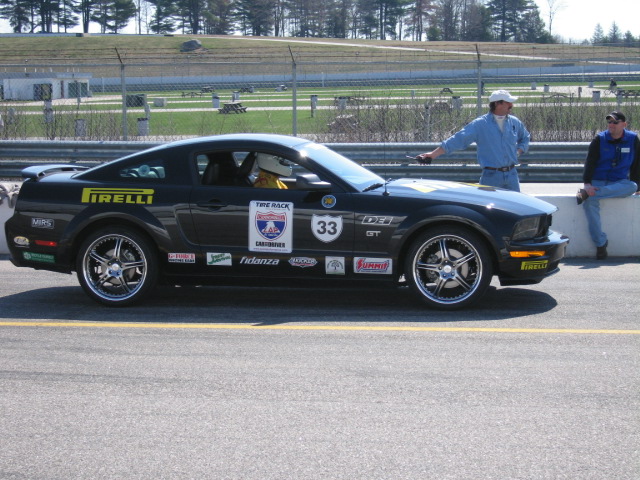 Black Ford Mustang GT with racing decals and number 33 on side. Driver in helmet visible