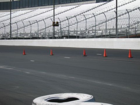 1991 Ford LTD Crown Victoria - A race track scene with orange cones marking a path, and empty grandstands visible beyond the track.