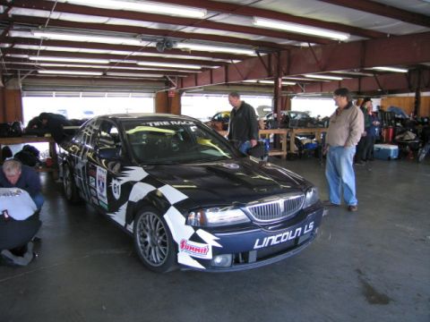 1991 Ford LTD Crown Victoria - A Lincoln LS race car is parked in a garage bay with people around it.