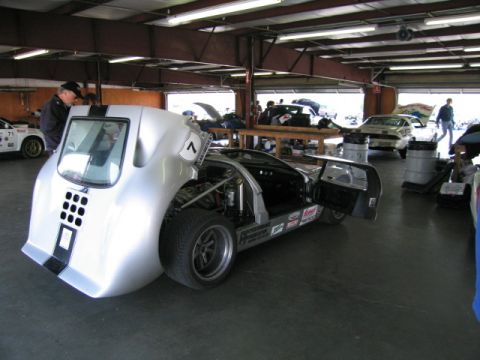 1991 Ford LTD Crown Victoria - A silver race car is parked in a garage with other vehicles and people around.