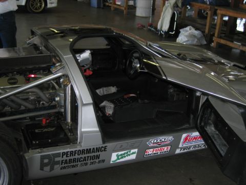 1991 Ford LTD Crown Victoria - Interior view of a custom silver race car, showing exposed engine components and various racing decals on the door sill.