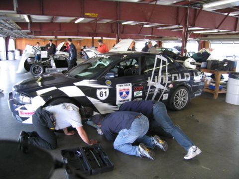 1991 Ford LTD Crown Victoria - Crew members work on a race car in the pit garage, with another vehicle in the background.