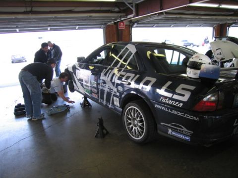 1991 Ford LTD Crown Victoria - A Lincoln LS race car is being worked on in a garage, with "Lincoln LS" graphics and sponsor decals visible.