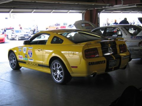 1991 Ford LTD Crown Victoria - Yellow 2005 Ford Mustang with racing stripes and 'Ford Racing' decals parked in a garage.