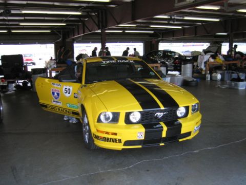 1991 Ford LTD Crown Victoria - A yellow Ford Mustang with racing decals sits in a garage with its door open.