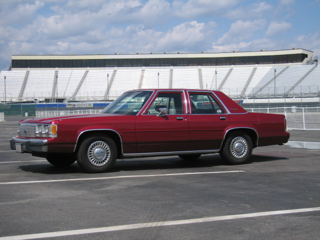 Red sedan parked on asphalt with stadium seating in the background