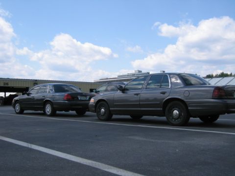 1991 Ford LTD Crown Victoria - Two police sedans are parked in a lot under a cloudy sky.