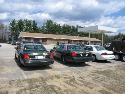 1991 Ford LTD Crown Victoria - Several police vehicles are parked in front of a building with a covered gas station canopy overhead.