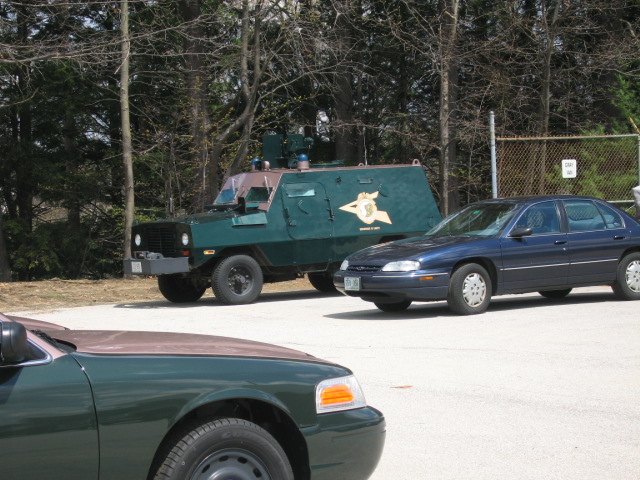 Armored vehicle and two sedans parked in a lot