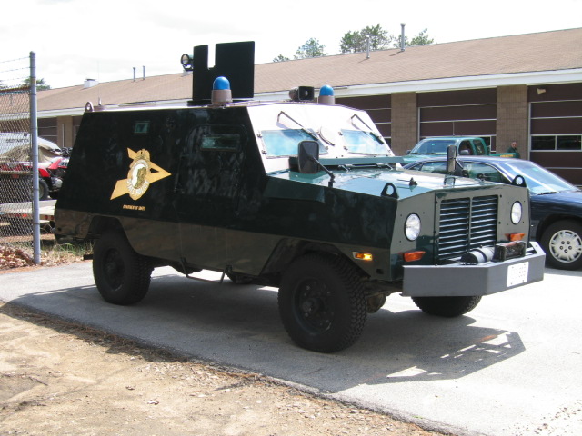 Green armored vehicle with a yellow emblem on the side, parked on asphalt