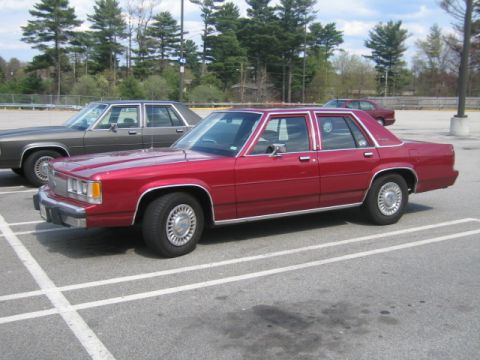 1991 Ford LTD Crown Victoria - A red sedan is parked in a lot next to another car. The vehicle appears to be from the early 1990s.