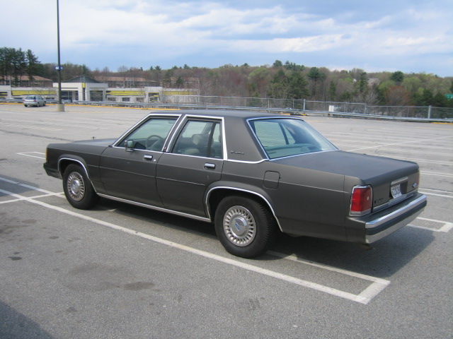 Dark gray 1980s Ford sedan parked in a lot, rear 3/4 view