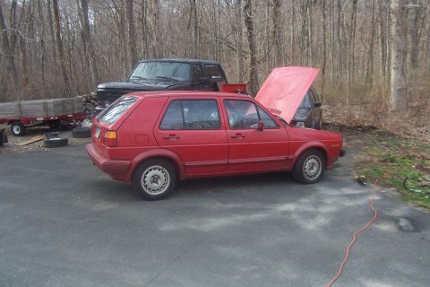 1996 Ford Bronco - A red Volkswagen Golf is parked outside with its hood open, next to a black Jeep and a trailer.
