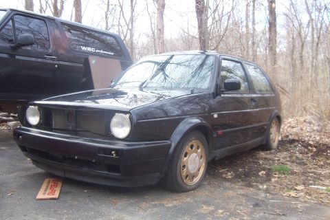1996 Ford Bronco - A black Volkswagen Golf GTI is parked outdoors next to a large black SUV, with trees in the background.
