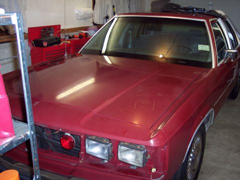 2001 Ford Crown Victoria - A red 2001 Ford Crown Victoria is parked in a garage, showing its front end with scribbled markings on the hood.