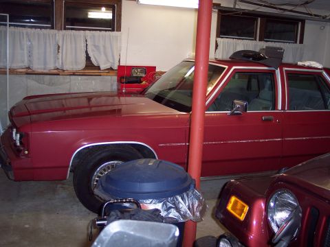 2001 Ford Crown Victoria - A red sedan is parked in a garage next to another vehicle.