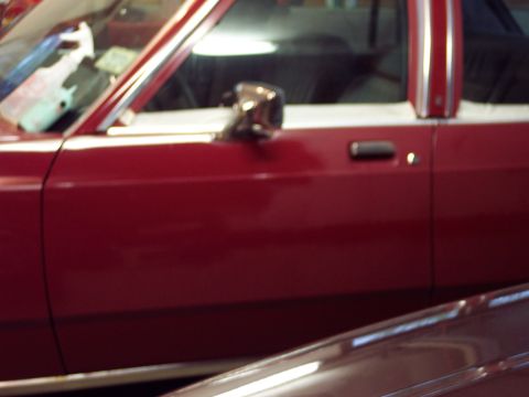 2001 Ford Crown Victoria - A close-up view of a red car's side door and mirror, with another vehicle in the foreground.