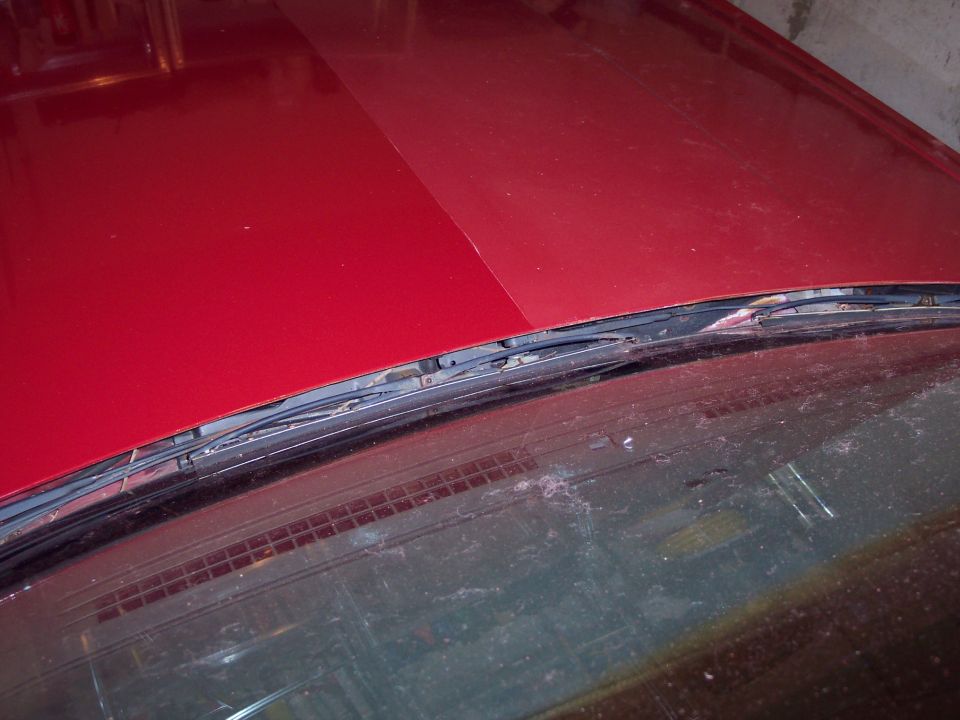 Red car hood with visible seam, windshield wipers, and dirty windshield