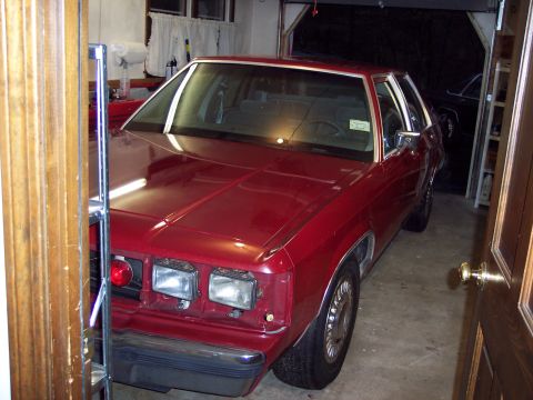 2001 Ford Crown Victoria - A red sedan sits in a garage, partially obscuring another vehicle in the background.
