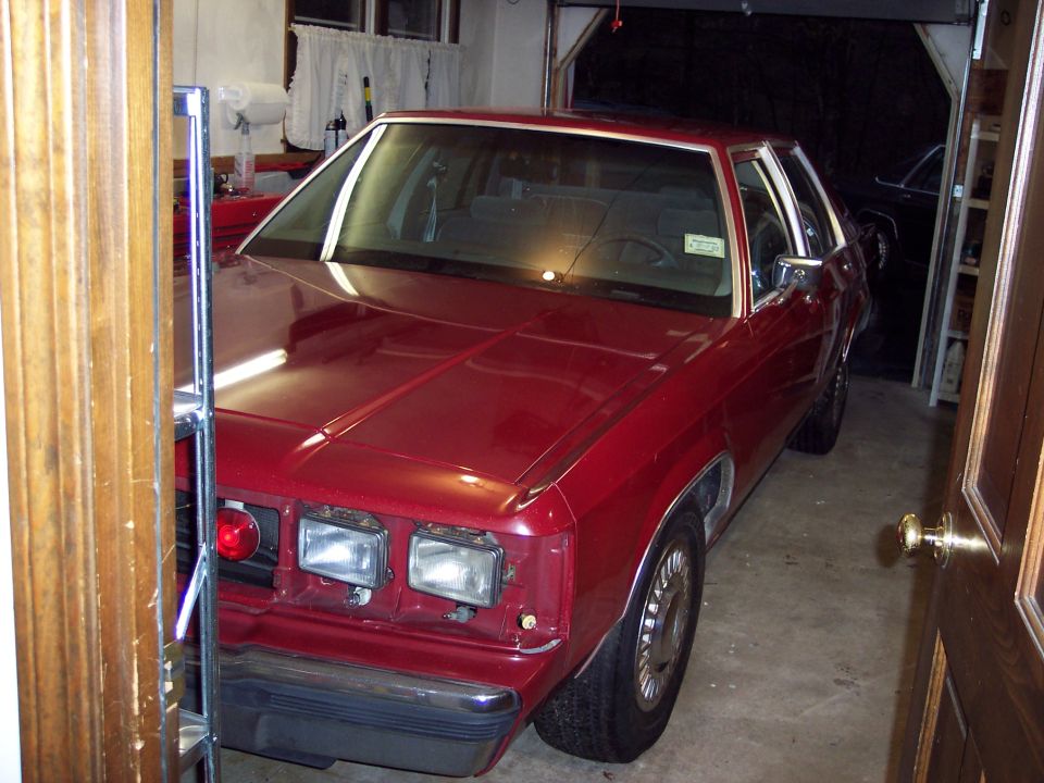 Red sedan parked in a garage, another dark vehicle visible in the background