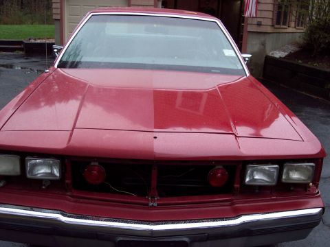2001 Ford Crown Victoria - The front of a red car is shown, square headlights and a grille that appears to be missing some components.